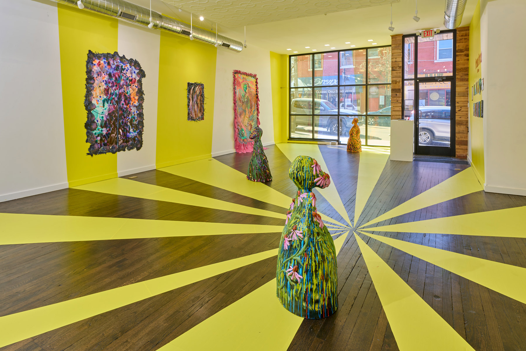 Installation of my exhibition, Present Portal. There are three large-scale ceramic works and four paintings. The floor and window are covered in yellow vinyl patterns which mimic beams of light. These beams extend to the walls where they are hand painted.