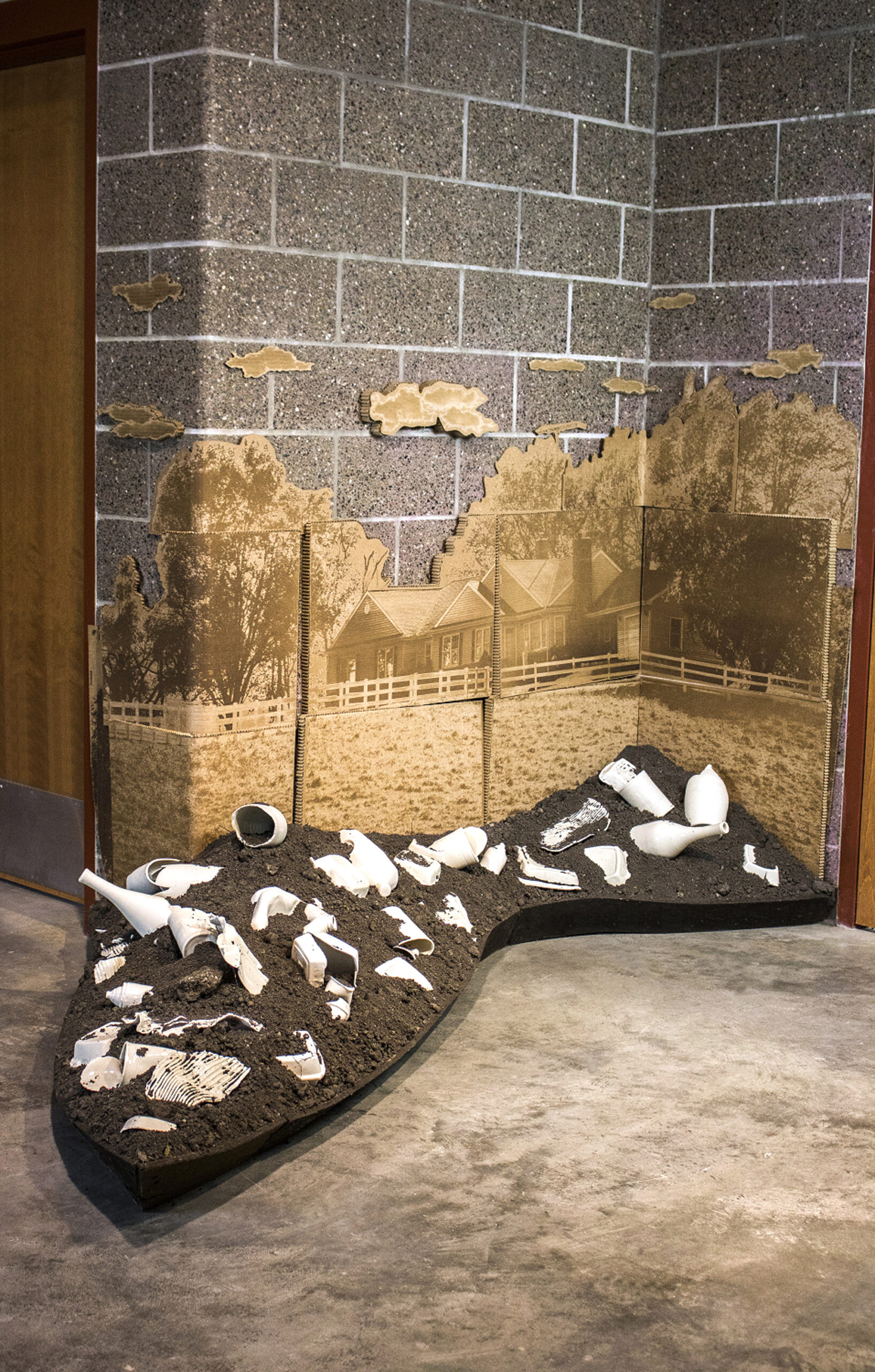 Porcelain objects embedded in dirt in front of laser etched cardboard.