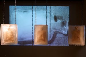 Silent Scream is a durational and immersive ceramics and video installation. The impending shatter of clay bodies frozen in ice, presents a sense of contingency and precariousness in viewers, the anticipation of fracture. As the ice melts the body of the bottle slowly reveals itself, and as if gazing into the disappearing haze of a clouded mirror you begin to see yourself: an empty vessel, headless, perhaps heedless, with gaping mouth frozen into a silent scream. Here the systemic failures, fragilities and unpredictability of living in this historical moment is felt bone-deep before the truth of it is fully, mindfully apprehended.