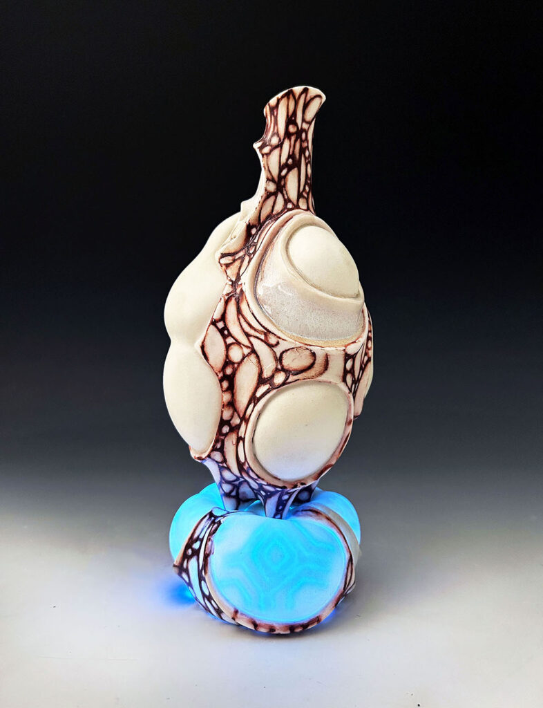 A  pitcher sits atop a porcelain platform that lights up with a controller. When the platform glows, a hidden pattern displays. The red surface is hand-painted and inspired by lattice structures found on insect wings. LED lights are hidden and connected to a rechargeable battery.