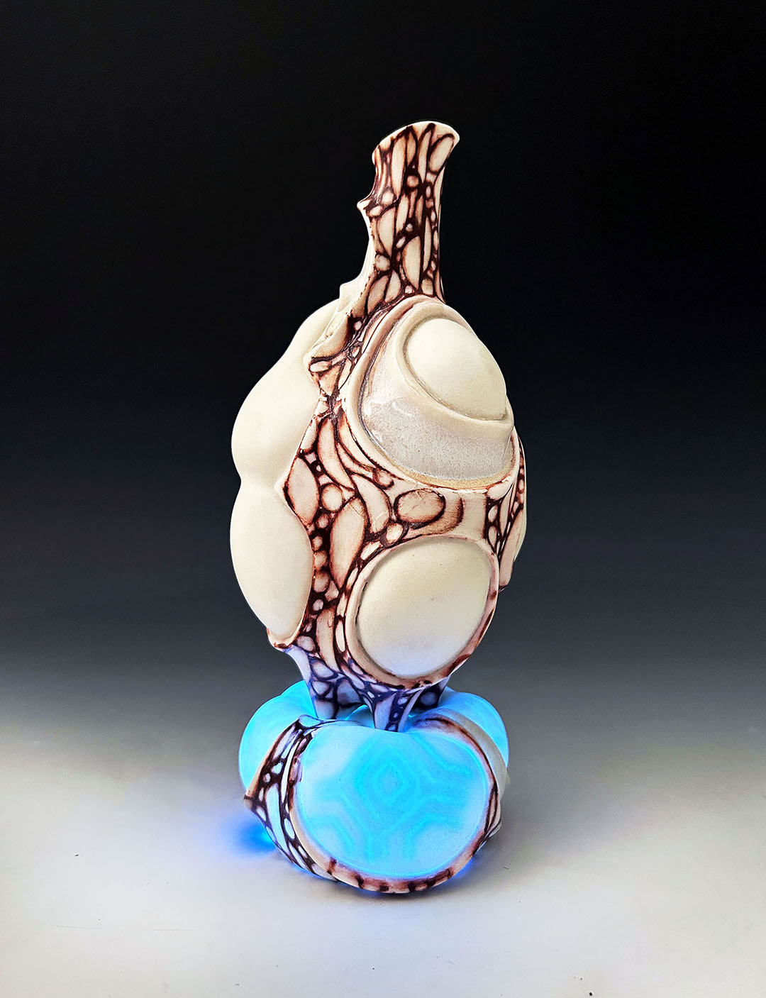 A  pitcher sits atop a porcelain platform that lights up with a controller. When the platform glows, a hidden pattern displays. The red surface is hand-painted and inspired by lattice structures found on insect wings. LED lights are hidden and connected to a rechargeable battery.