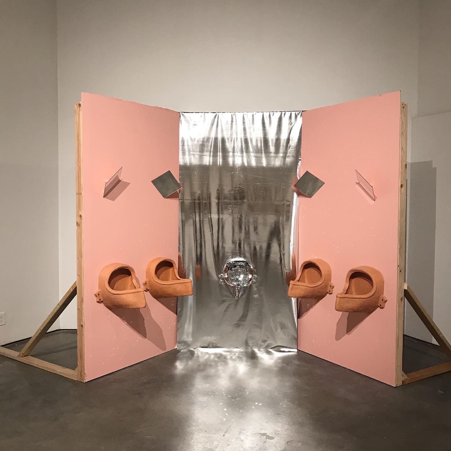 2020, terracotta, disco ball mirror, vinyl, latex, drywall, wood

I am interested in the identity duality of a mascuine born body, and its relation to the spaces that it specifically has to exist in, creating a space that is both hyper personal and extremely detached.I want to explore this part of my identity that I am tied to because of my male born body and how being raised in that way and how those spaces influenced how I developed an understanding of myself. 
The public bathroom is a public and private space. The Urinal is designed for the use of male born bodies, and In the development of a male person's identity they become a sort of rite of passage into “manhood.”  In itself the urinal is just a vessel, or depository for a human's by-product but in its layout, design, usual proximity to one another forces a confrontation and examination. The public bathroom becomes a stage and an arena for the performability to one's masculinity, forcing comparisons.