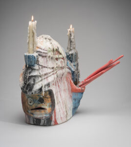Handbuilt object with a small face and two candles melting all down the object.