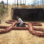 Site Specific, 2013, Recycled red clay, volcanic rock, performer in white, pine charred by recent forest fires, red cord, black adobe, and coal