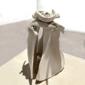 An alter is constructed from three cow scapulas tipped up and leaning into a pyramid shape, with a birds nest made of bent cow ribs and porcelain grass perched on top. Inside the nest, the skull, furcula (wishbone), and leg bones rest. The piece is sitting on a light wood pedestal in a white walled gallery with grey floors.