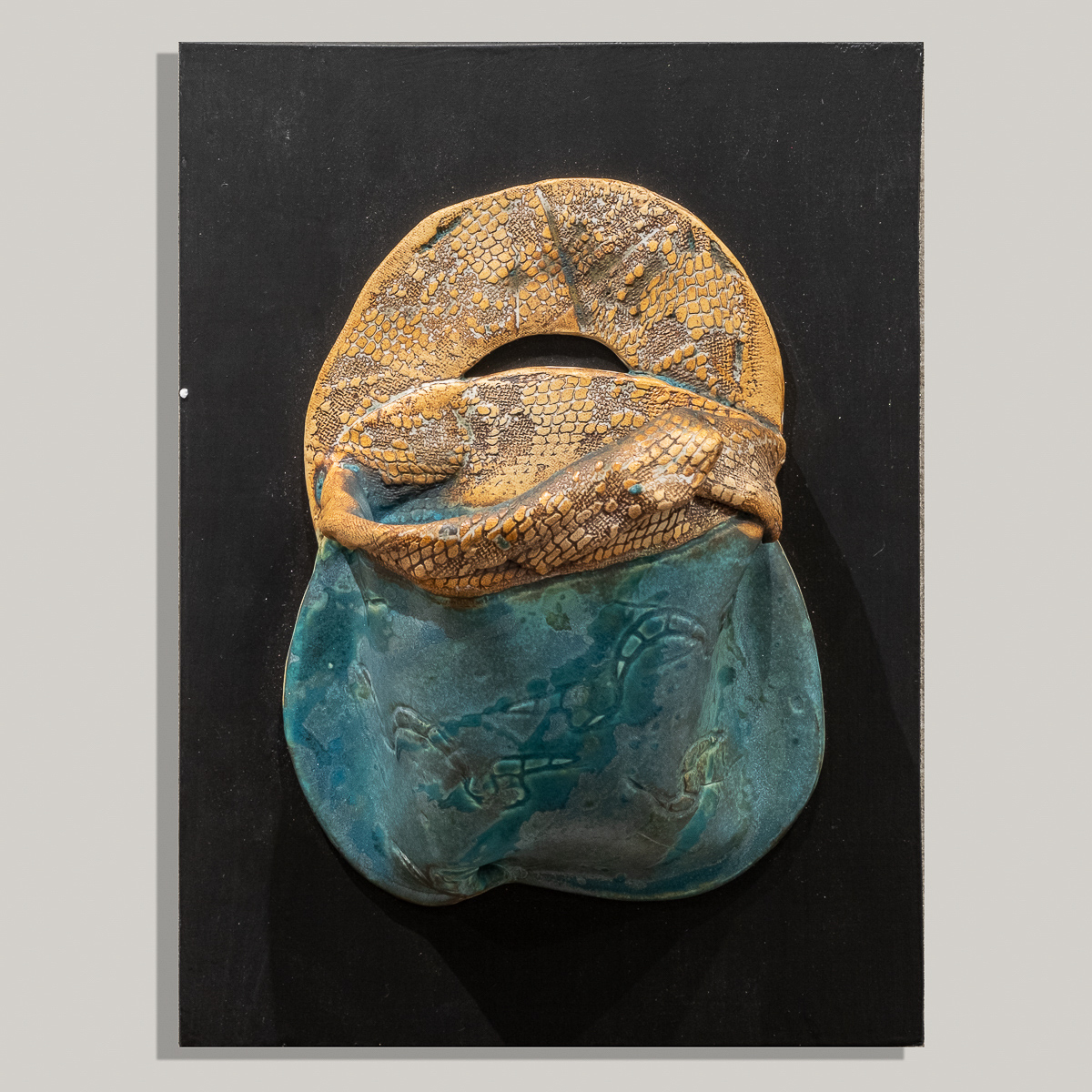Stoneware wall pouch is highly textured with material and slab built.  Red iron oxide stain is painted on handle and top of pouch  and then wiped off to highlight the texture made by pressing  lace patterns onto the clay. Inside of the pouch and bottom are glazed in my turquoise semi- matte glaze. Fired to cone 6 in oxidation and mounted on painted wood that is wired on the back to hang on the wall like a painting. Can hold water to display fresh flowers.