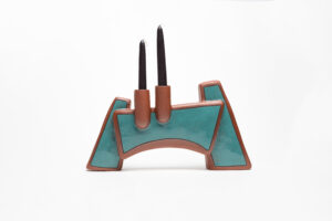 The part of the candelabra that holds the candles is wheelthrown, attached to a larger slab built form. The majority of this piece is unglazed with terra sigilata, a portion is glazed teal/blue. There is a black inlayed line surrounding the glazed portion. Cone 1.