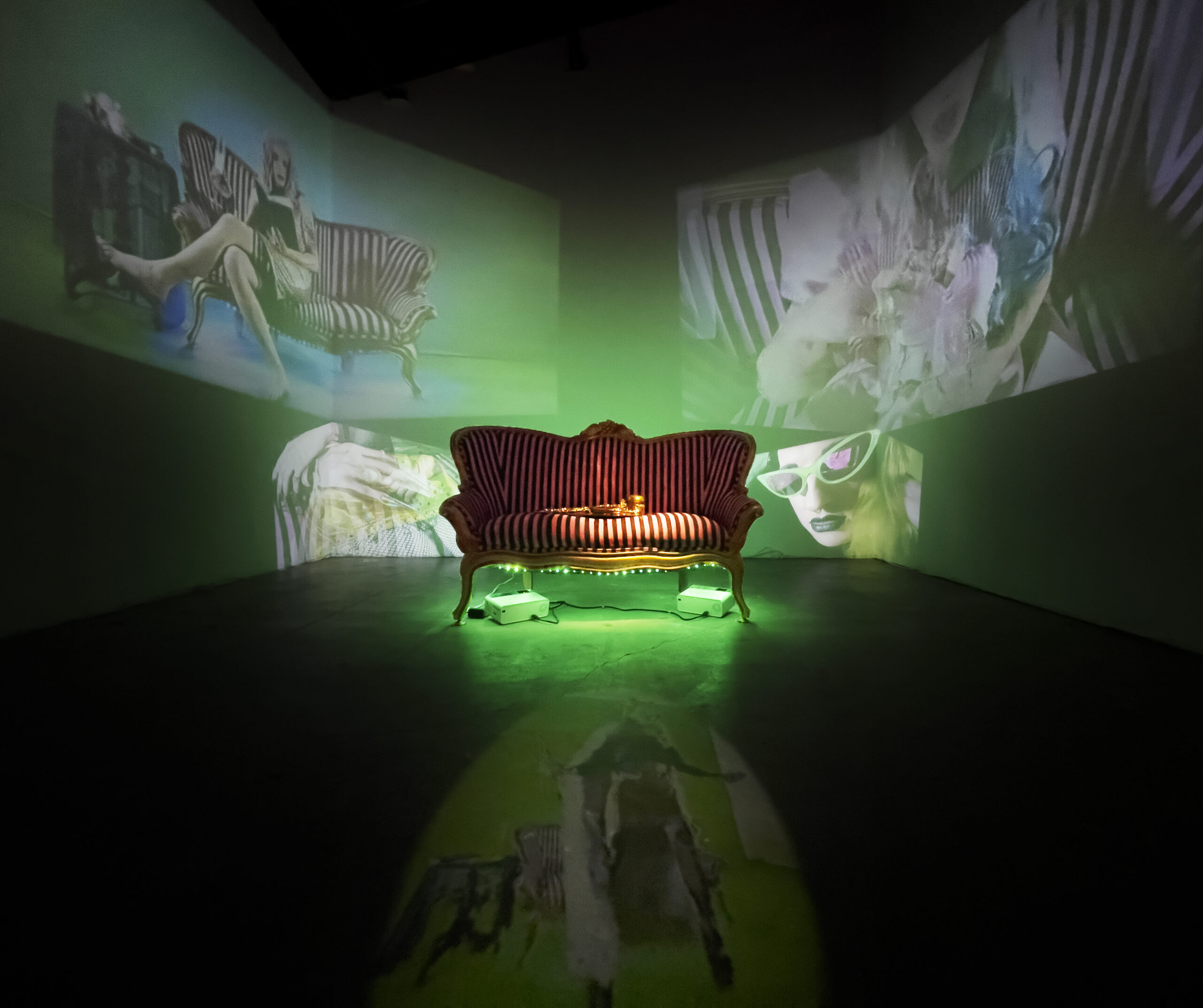 2021, 6 Projected Video, Couch, Terracotta. 

While the north space focuses on the Diva and the performance of gender and identity, it dehumanizes me, the south gallery works to re-humanizes me. The variation of close ups, angles, and subject matter works together to show a raw side of humanity: human desires, human actions, and sexuality. The south space exists within the past and as a transition out of the present. There is an undeniable presence of a stasis and waiting by the lounging bodies, and the never ending tapping of stiletto nails. While this space lies mostly within the realm of the interior, the acknowledgement of the viewer through the audio as well as the moments of locking eyes with the camera searching for eye contact on the other side speaks to a desire to be seen, foreshadowing what is to come within the near future.