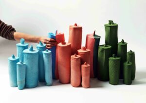 Soft cellulose sponge molds are mixed into the installation. A hand is squeezing the molds to differentiate them from the colored porcelain pieces.