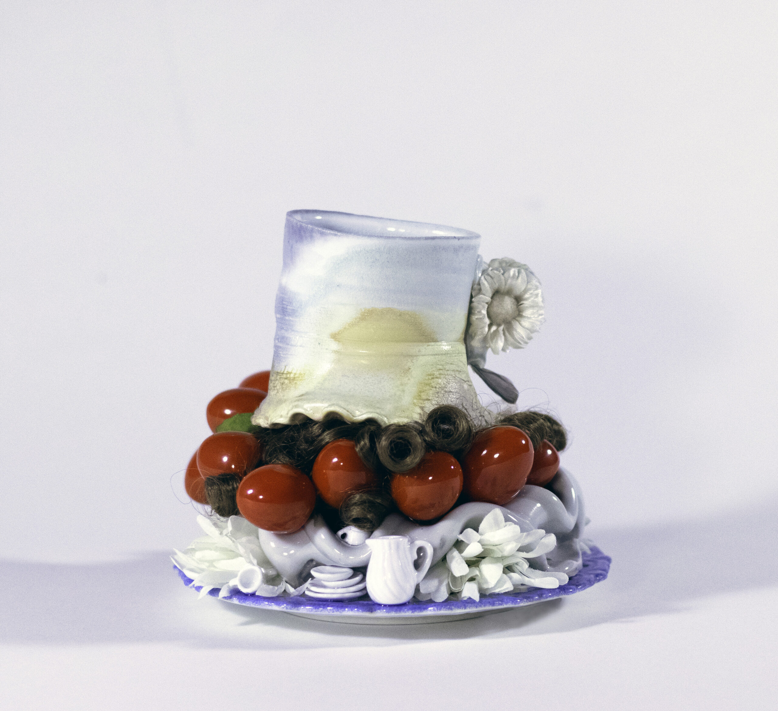 This piece explores the paradox between the function of food and the purpose of ornament. 
Can nourishment a traditionally functional medium become an ornament? Who might want this and for what purposes?

Cup and Saucer explores the history of ceramics in both firing processes and clay as art. A timeline from ancient woodfiring methods, to gas reduction, to industrial ware with decals is displayed; a functional cup sits a top (or is supported by) a rorschachian sculpture- resting on a decorative industrial plate. 

A doll set of dishes speaks of a game to be played, or due to the scale of the pitcher to the actual teacup- a problem to be solved. By intentionally engaging multiple perspectives, the artist leaves the choice of how to understand the dilemma to the viewer.