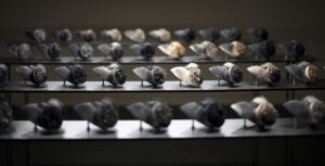 The installation presents a collection of 40 individual porcelain gas masks fired individually in sagger boxes with carbon at 1260 °C. Each mask is unique and it has a very intricate handmade flower work on the vents. 
Using the nature of smoke, fire and heat to create blooms of colour and distinctive markings across the surface of the porcelain, producing spontaneous and unpredictable effects.This work can be sold individually or as an installation with a group of them.