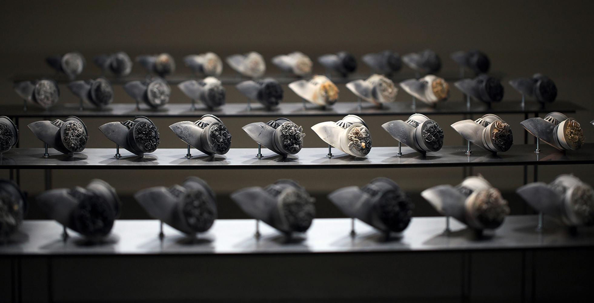 The installation presents a collection of 40 individual porcelain gas masks fired individually in sagger boxes with carbon at 1260 °C. Each mask is unique and it has a very intricate handmade flower work on the vents. 
Using the nature of smoke, fire and heat to create blooms of colour and distinctive markings across the surface of the porcelain, producing spontaneous and unpredictable effects.This work can be sold individually or as an installation with a group of them.