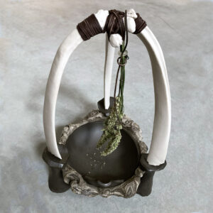 A sculptural Vessel made for seed drying and saving. Comprised of a deep iron rich clay basin embedded in marbled clay and postconsumer glaze waste material, that is propped up on 3 mushroom like feat. The feat extend past the lip of the basin, and support three slip cast, white porcelain bones that are bound together at the top with leather lattice work, which allows the Anise Hyssops to dangle freely, dry and release its seeds into the basin. A little pour spout directs the seeds when ready to gather and deposit into a container for safe storage.